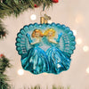 A glittery Christmas tree ornament shows two blonde women in blue gowns with the word SISTERS on each side, set against a blue seashell background. Green pine branches are visible around the ornament.