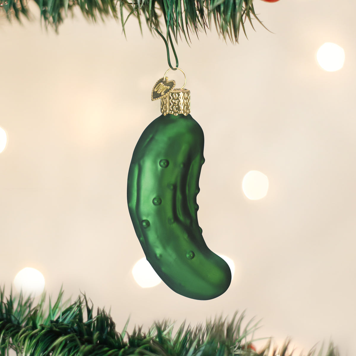Green pickle-shaped Christmas ornament hanging on a tree with lights in the background.