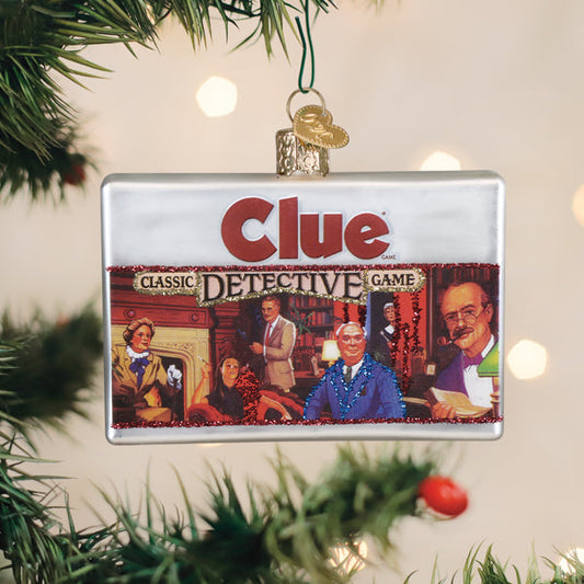 A rectangular Christmas tree ornament of the Clue board game box, featuring illustrated characters from the game and the text â€œClue: Classic Detective Game, hanging on a tree with green branches and blurred lights.